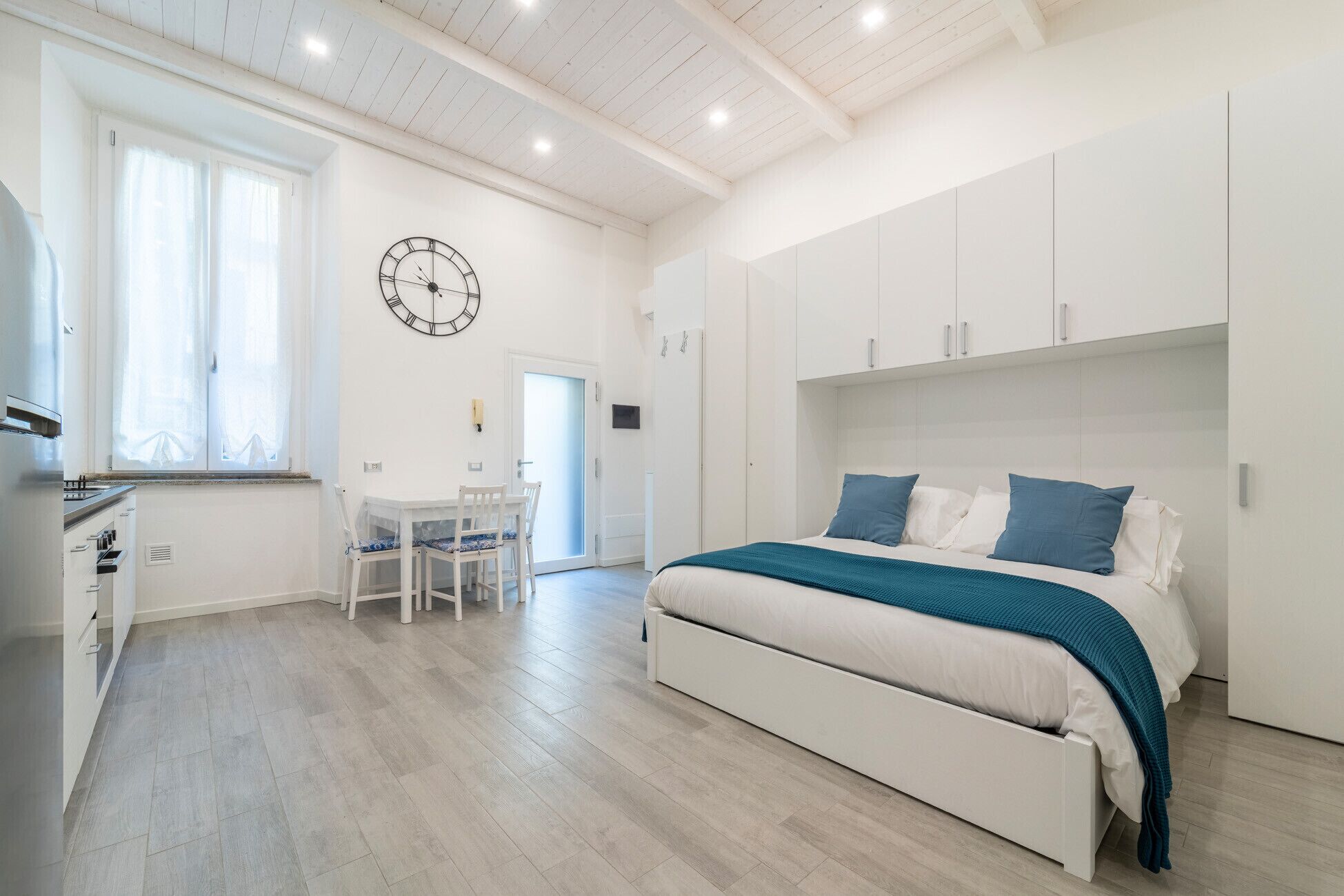Quarto com cama, mesas de cabeceira e relógio na parede.
