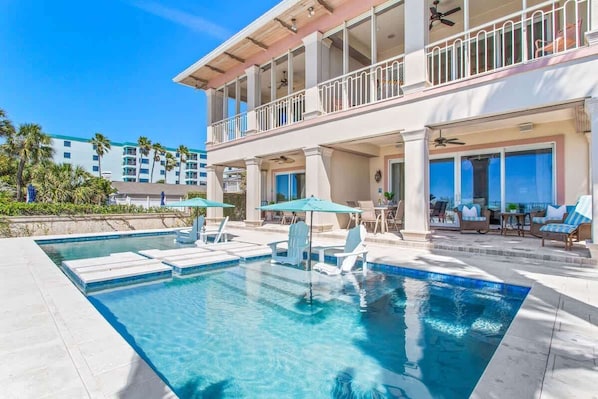 A pool area with lounge chairs, a covered seating area, and a two-story building with balconies.