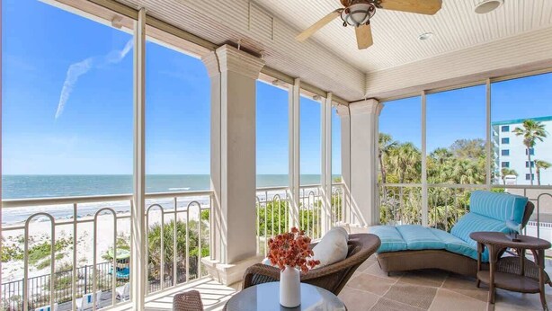 Espaço coberto ao ar livre com vista para a praia, móveis de vime e um ventilador de teto.