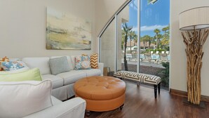 Un salon moderne avec une grande fenêtre, un canapé, un pouf et une lampe décorative.