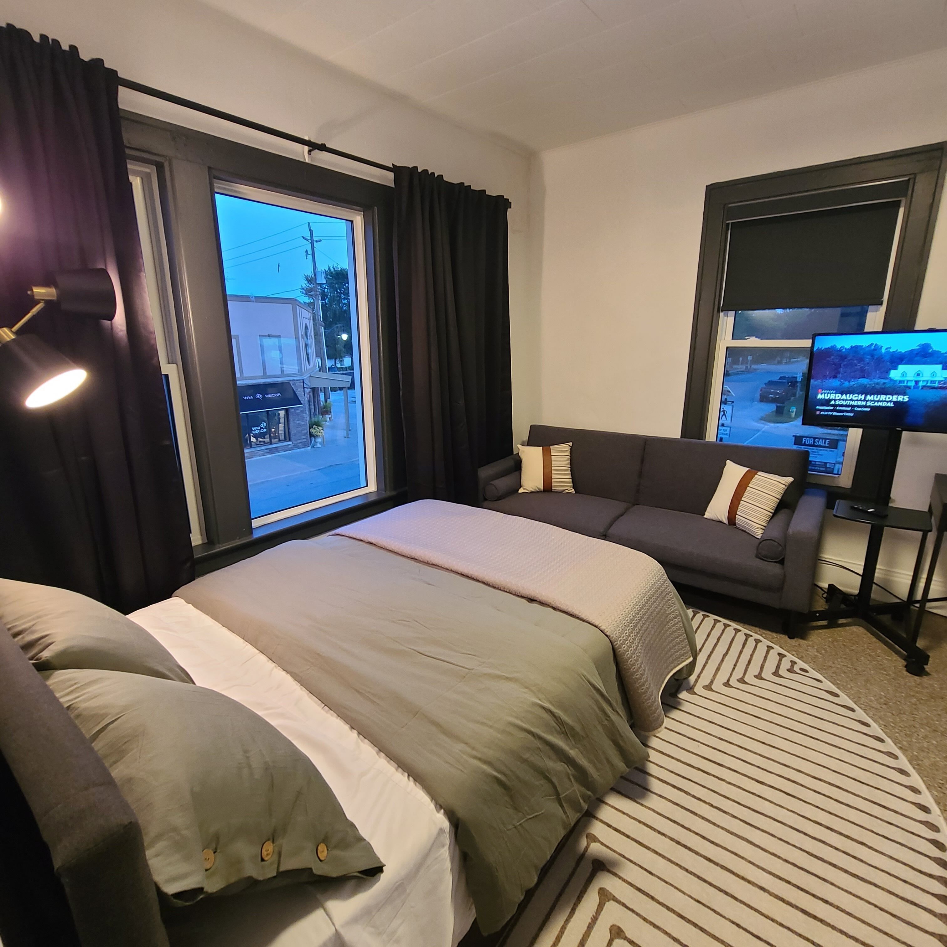 Habitación de hotel con cama, sofá, televisión y vista a la calle.