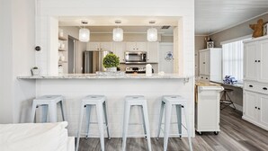 Una cocina moderna con armarios blancos, electrodomésticos de acero inoxidable y una isla central con taburetes de bar.