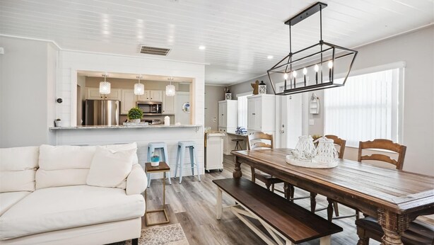 Una cocina moderna con armarios blancos, un comedor con mesa y bancos de madera, y un sofá blanco.