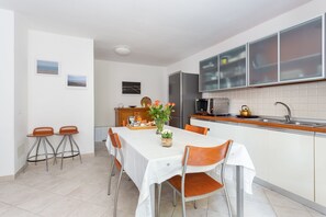 A modern kitchen with white cabinets, a stainless steel refrigerator, and a wooden countertop. There is a dining table with chairs and a vase of flowers. - Beautiful and spacious apartment for families in Gallura (Tempio Pausania)