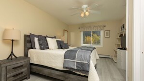 A bedroom with a bed, bedside lamp, ceiling fan, window with curtains, and a dresser. - Woodbridge Inn Retreat: Perfect Frisco Location (Frisco)
