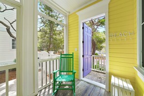 Un porche avec une chaise verte, une porte violette et un mur jaune sur lequel on peut lire l’inscription « PLAGE ».