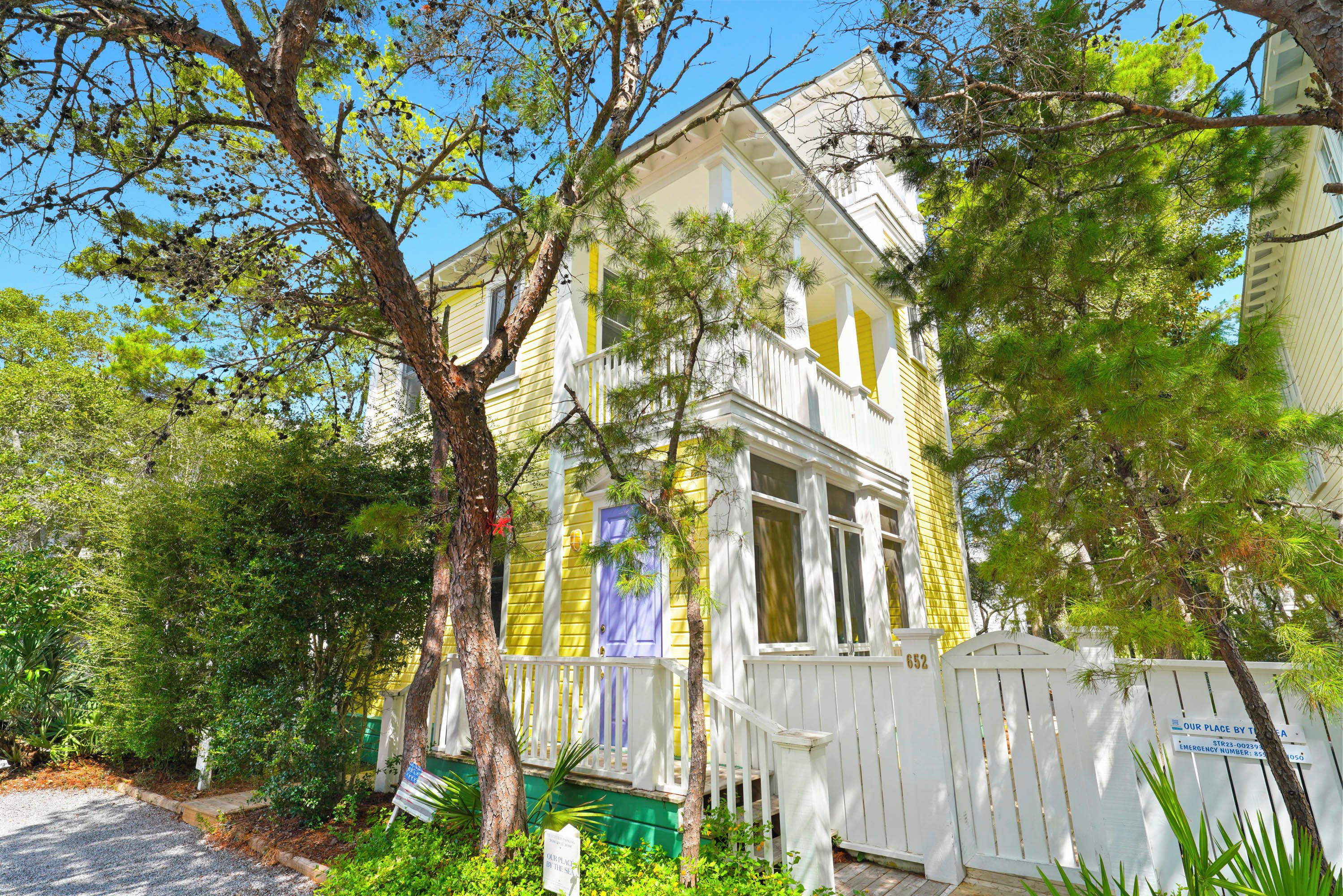 A two-story house with a white picket fence, a porch with a purple door, and a mailbox.