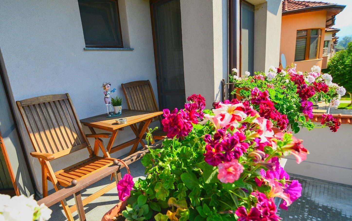 A balcony with wooden furniture, potted plants, and a view of a building.