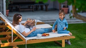 Eine Frau und ein Kind sitzen draußen auf einer Holzliege bei einem Picknick, mit Essen und einer Tasse.
