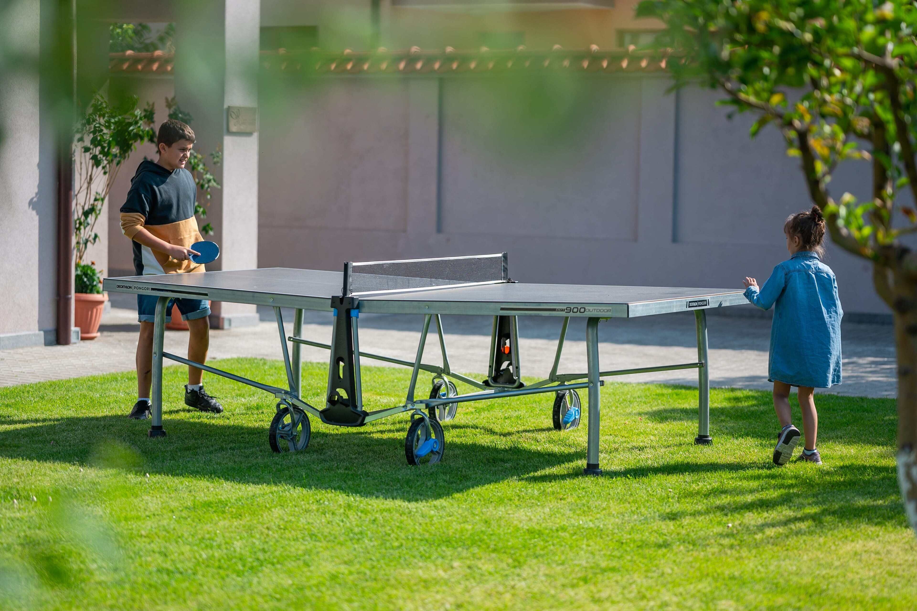 A portable ping pong table on a grassy area with a building in the background.