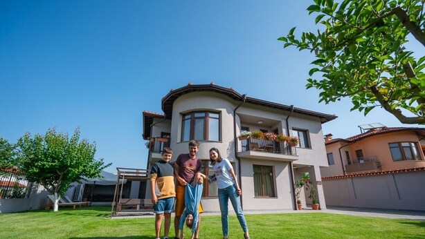 Ein modernes, zweistöckiges Haus mit gewölbter Dachlinie, einem Balkon mit Topfpflanzen und einem gepflegten Rasen.
