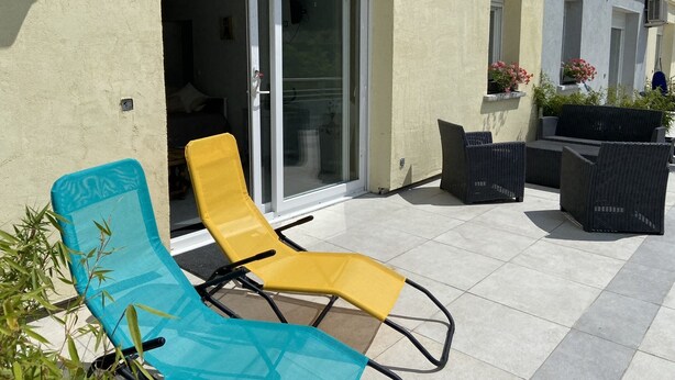 Un patio con mobiliario exterior, una puerta corrediza de vidrio y plantas en macetas.
