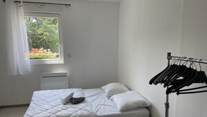 Un dormitorio pequeño y limpio con una cama individual, una ventana con vistas a la vegetación y un tendedero.