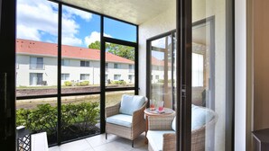 Een balkon met rieten meubels, een glazen tafel en uitzicht op een gebouw met een rood dak.