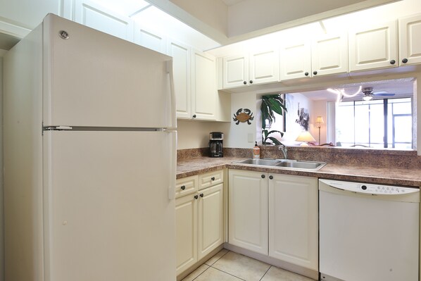 A kitchen with white cabinets, a refrigerator, a dishwasher, a coffee maker, and a sink.