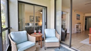 Een balkon met rieten stoelen en een kleine tafel, een schuifglazen deur naar een slaapkamer en uitzicht op de omgeving.