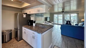 A modern kitchen with white cabinets, a granite countertop, a stainless steel refrigerator, and a coffee maker.