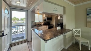 A kitchen with a granite countertop, white cabinets, a microwave, and a sign indicating 'BEACH HOUSE'.