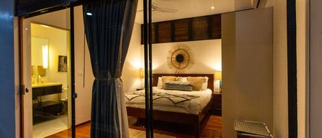 A modern bedroom with a large bed, a nightstand, a wall-mounted lamp, and a window with curtains.