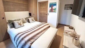 A bedroom with a wooden headboard, a bed with a striped blanket, and a small bedside table with a vase.