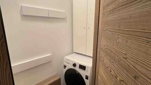 A compact laundry room with a washing machine, a cabinet, and a shelf.