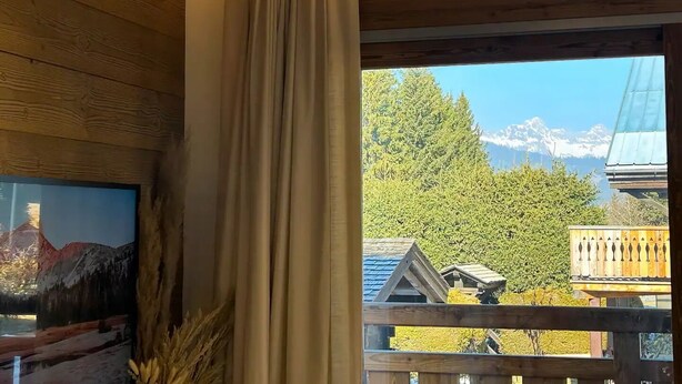 A room with wooden walls, a large window with curtains, and a painting on the wall.