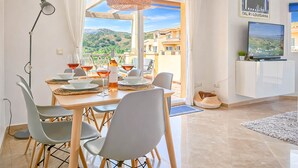 Un comedor con una mesa preparada para dos, un televisor en un mueble y vistas al campo.