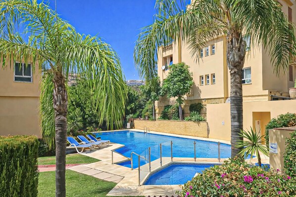A swimming pool surrounded by palm trees and a building with balconies.