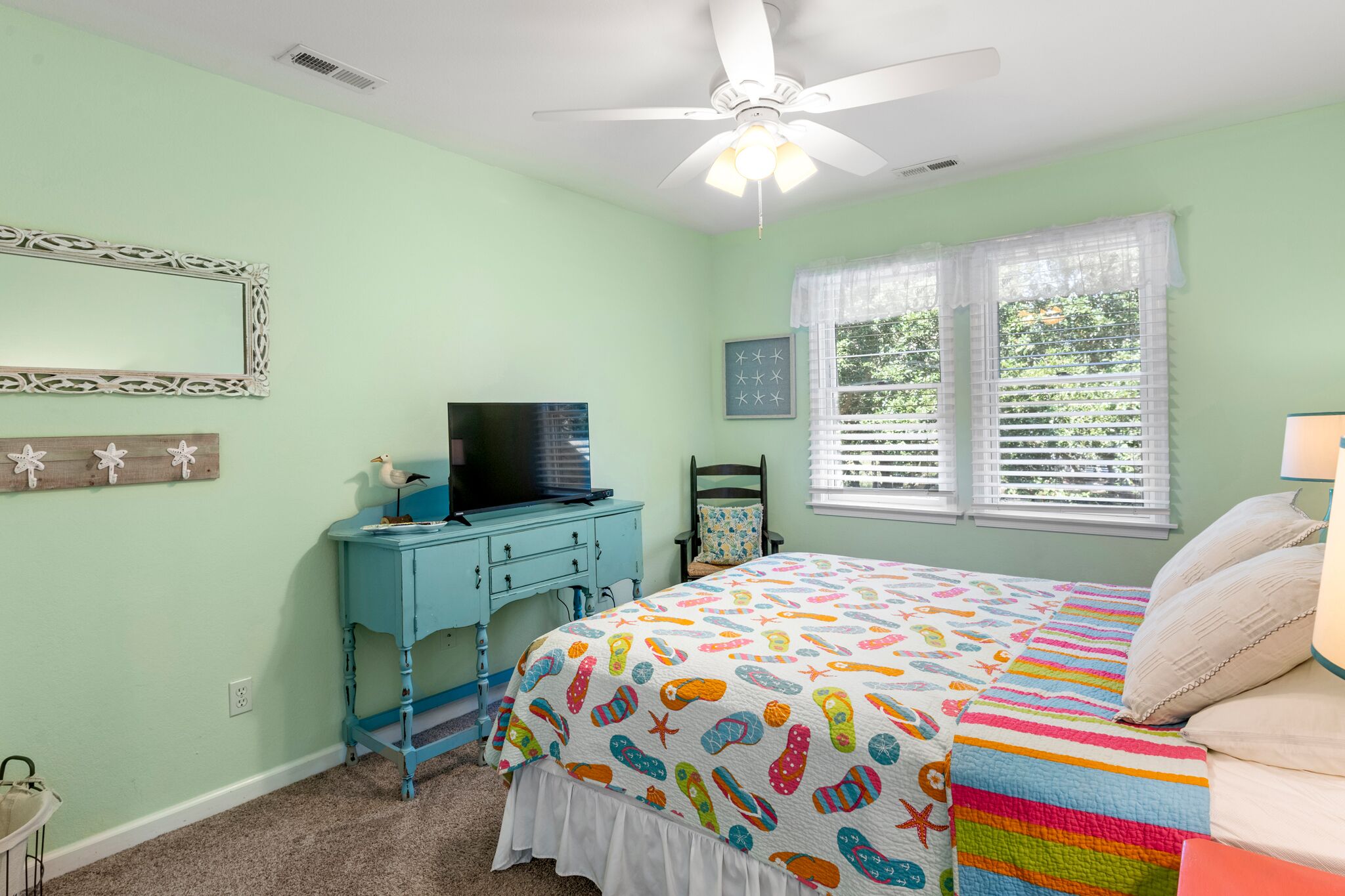 A bedroom with a bed, a desk, a ceiling fan, and a window with blinds.