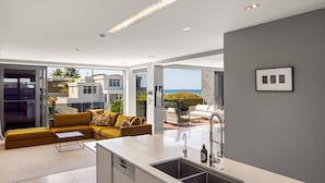 Una cocina moderna con una isla grande, una zona de comedor con un sofá amarillo y vistas al mar.