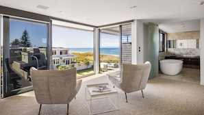 Un interior moderno con un amplio ventanal corredera que da a un balcón con vistas a la playa y al océano.