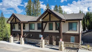Un chalet à deux étages, doté de fondations en pierre et de poutres en bois, avec de nombreuses fenêtres et un porche abrité.