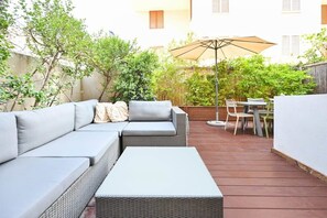 A patio with a grey sofa, a small table, and a dining area with chairs and a table.