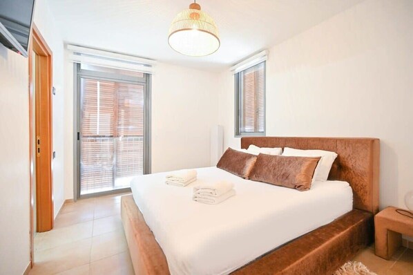 A bedroom with a large bed, a wooden headboard, a bedside table, and a hanging light fixture.