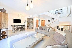 A modern living room with a sofa, coffee table, and dining area. There is a staircase leading to an upper level.