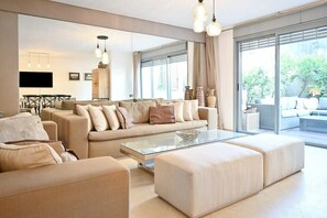 A modern living room with a sofa set, a glass coffee table, and a dining area with a TV and table.