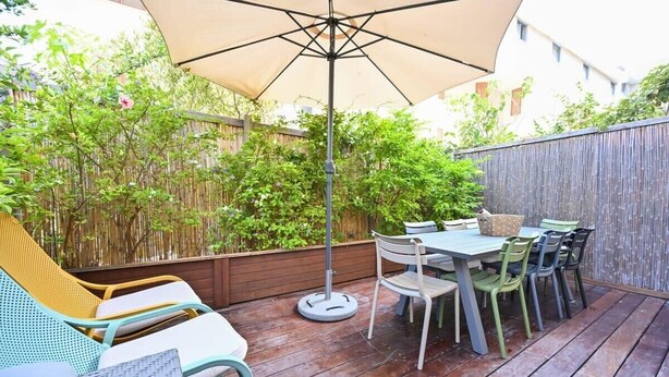 Un patio al aire libre con una mesa y sillas, una mesa redonda con toldo y un sillón de mimbre.