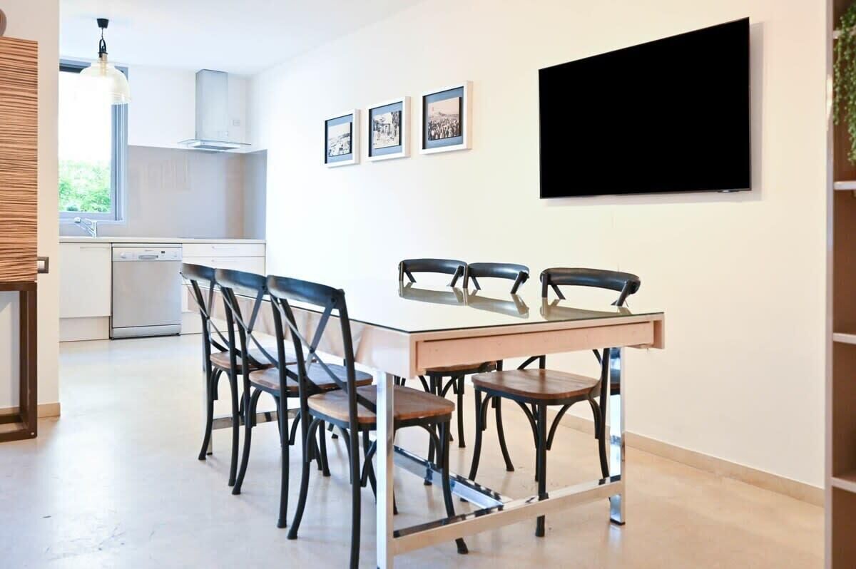 A modern kitchen with a dining area, a flat-screen TV, and framed pictures on the wall.