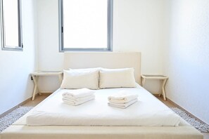 A minimalist bedroom with a large bed, two bedside tables, and a window.