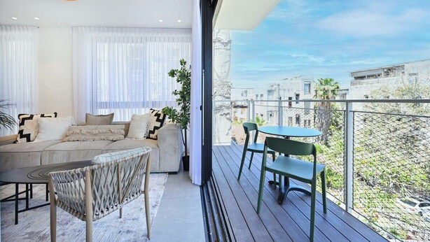 A modern living room with a sofa, chairs, and a table, connected to a balcony with a view of the city. - Sweet Home 3BR near the sea by HolyGuest (Tel Aviv-Yafo)