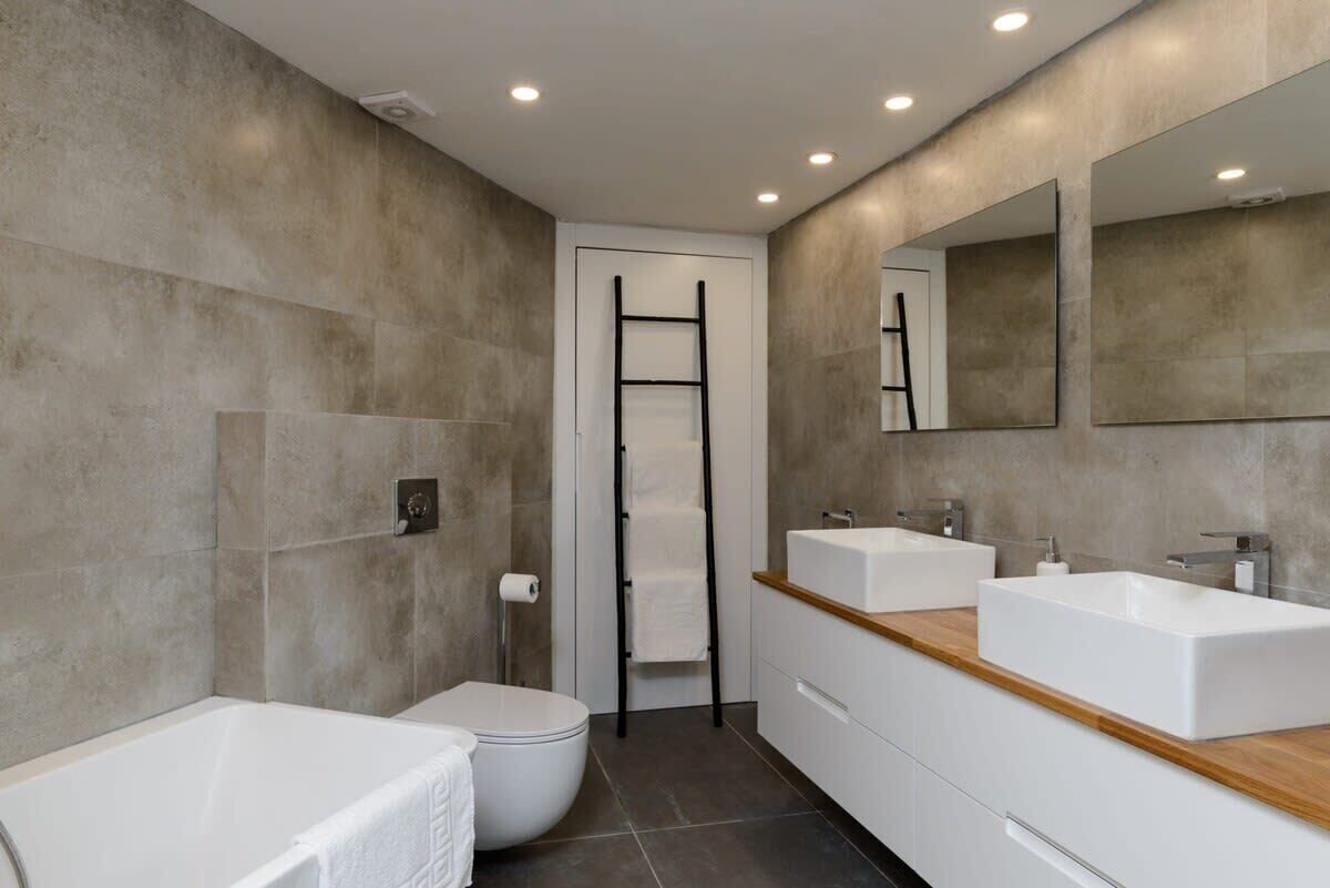 Une salle de bain moderne équipée d’une baignoire, de toilettes et de deux lavabos avec miroirs.
