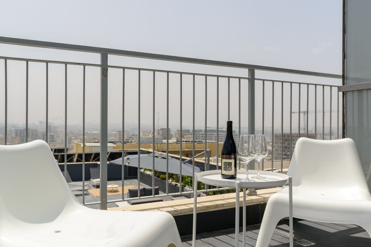 A rooftop terrace with a table, chairs, a bottle, and a glass.
