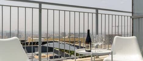 A rooftop terrace with a table, chairs, a bottle, and a glass.