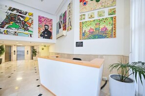 A reception area with a modern design, featuring a reception desk, a large abstract painting, and a potted plant.