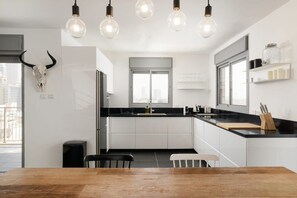 Una cocina moderna con armarios blancos, encimera negra y una mesa de comedor de madera. Hay bombillas colgantes y una decoración de cráneo de toro en la pared.