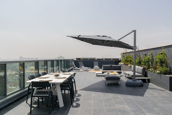 Una terraza en la azotea con comedor, zona de estar y una gran sombrilla.