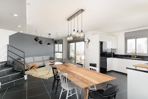 A modern kitchen with a wooden dining table, white chairs, and a staircase leading to a living area.