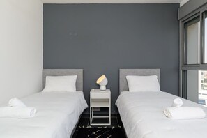 A hotel room with two beds, a nightstand with a lamp, and a view through a window.