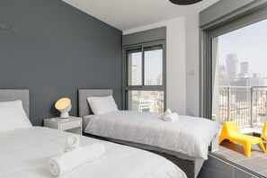 A modern hotel room with two beds, a large window with a city view, and a balcony with yellow chairs.