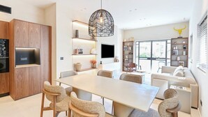 Une cuisine moderne dotée d’un four encastré, un coin repas avec une grande table et des chaises, et un salon avec un canapé et un téléviseur.
